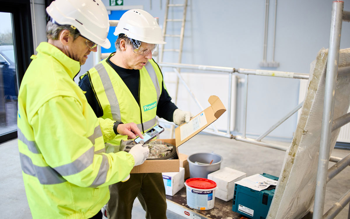 Man on the left is looking at Promat Firestopping Selector® App. The man beside him is reading from a clipboard.