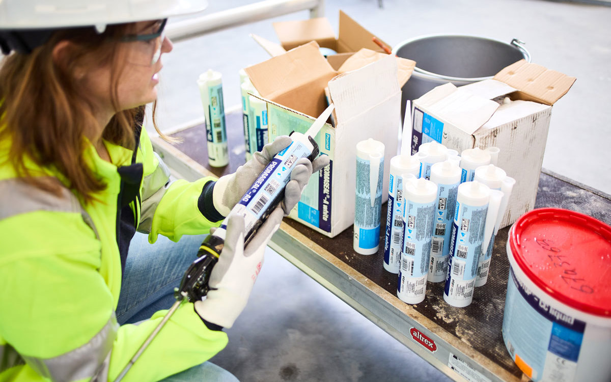 A woman installer reading the specifications on one of several sealant product and brand varieties before her.
