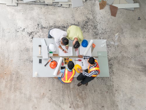 Pohľad zhora na štyroch projektantov pri práci okolo stola na stavbe