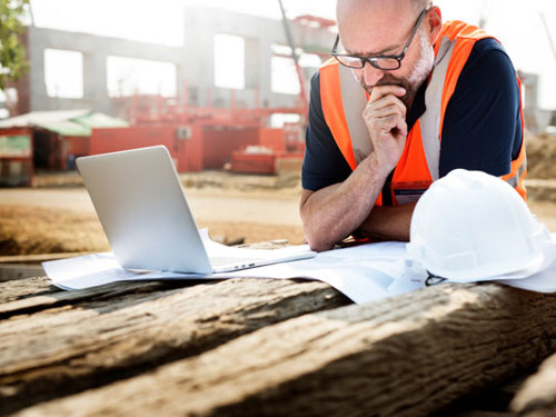 Muž zamyslene pracuje s laptopom na stavbe
