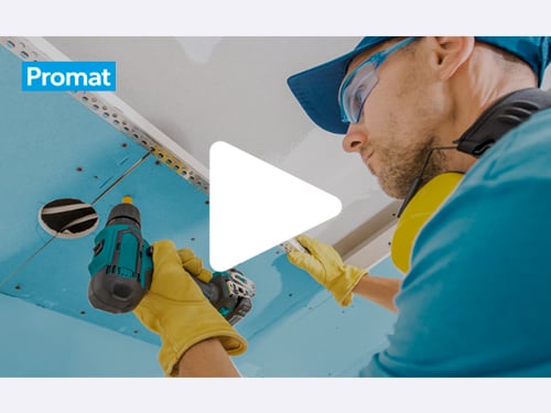 Slika zaslonskega zajema videa, v katerem delavec v modri majici, z zaščitnimi očali in rumenimi rokavicami, na strop vgrajuje modro obarvano požarno ploščo. 