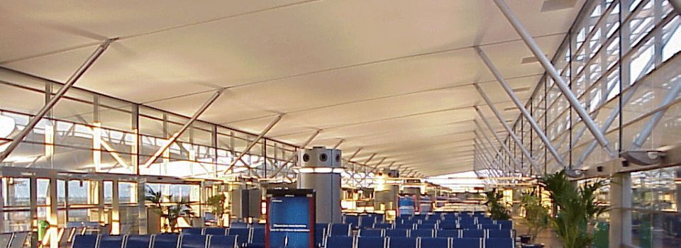 Čakacia hala na letisku s modrými stoličkami a protipožiarne chráneným stropom