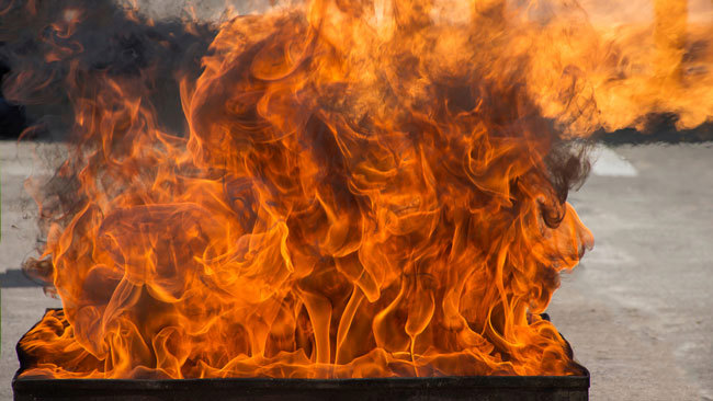 Slika velikega plamena, ki se vije iz zabojnika z gorečim bencinom.