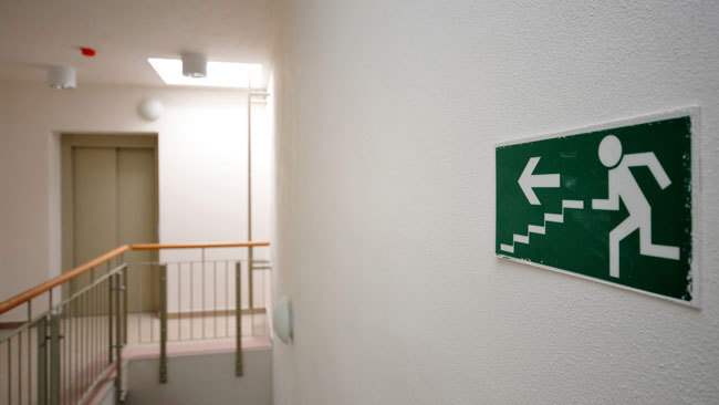 Slika prikazuje znak za put za evakuaciju postavljen u hodniku zgrade
