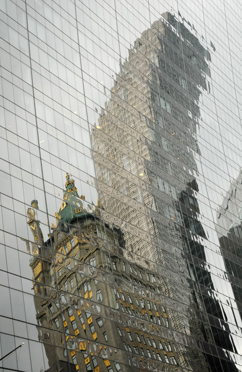 Két egymással szemközti épület torzított tükröződése egy másik épület üveghomlokzatán