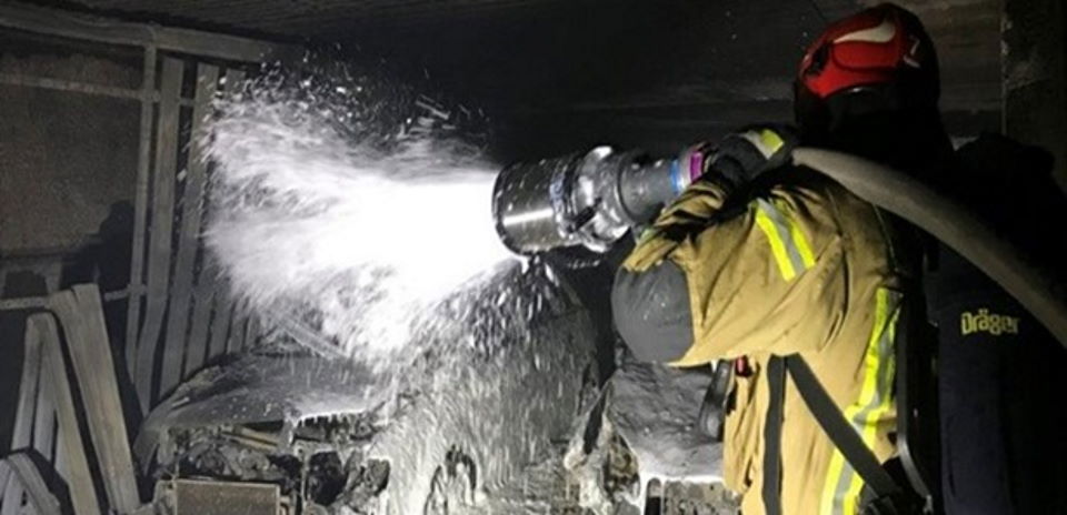 A fireman is putting out a recurring fire in a garage.