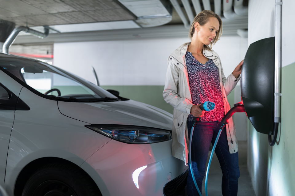 Woman getting ready to plug in her electric car into a wall charger in an underground garage.