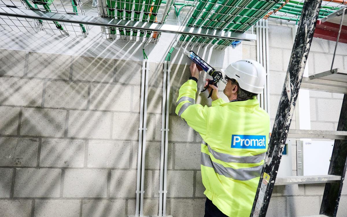 Čovek  u podrumu nanosi materijal na otvor gde se iza njega nalaze merdevine a ispred njega električna instalacija.