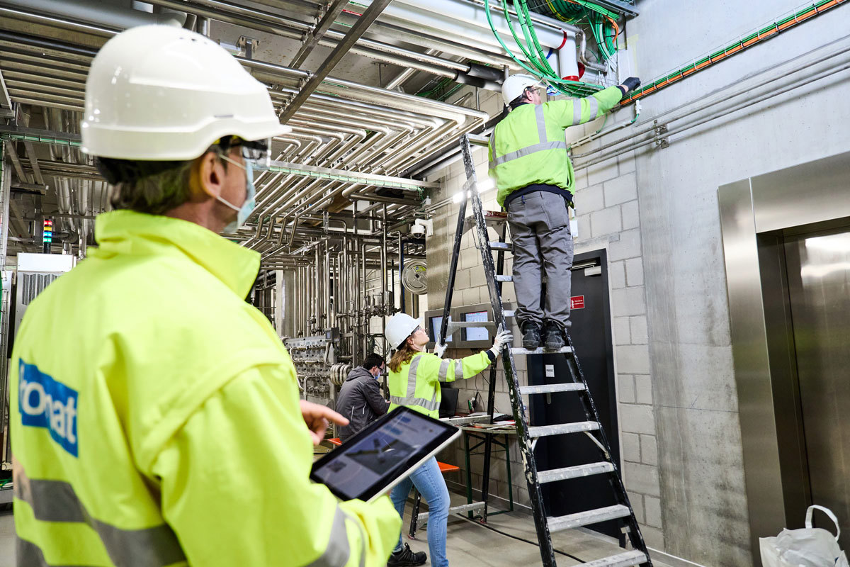 A man with a tablet looking at 3 installers installing penetration seals using PROMAT®coatings and sealants.