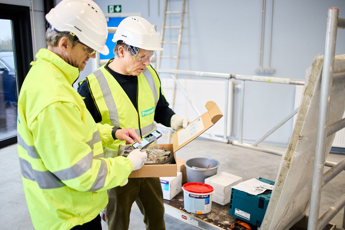 Man on the left is looking at Promat Firestopping Selector® App. The man beside him is reading from a clipboard.