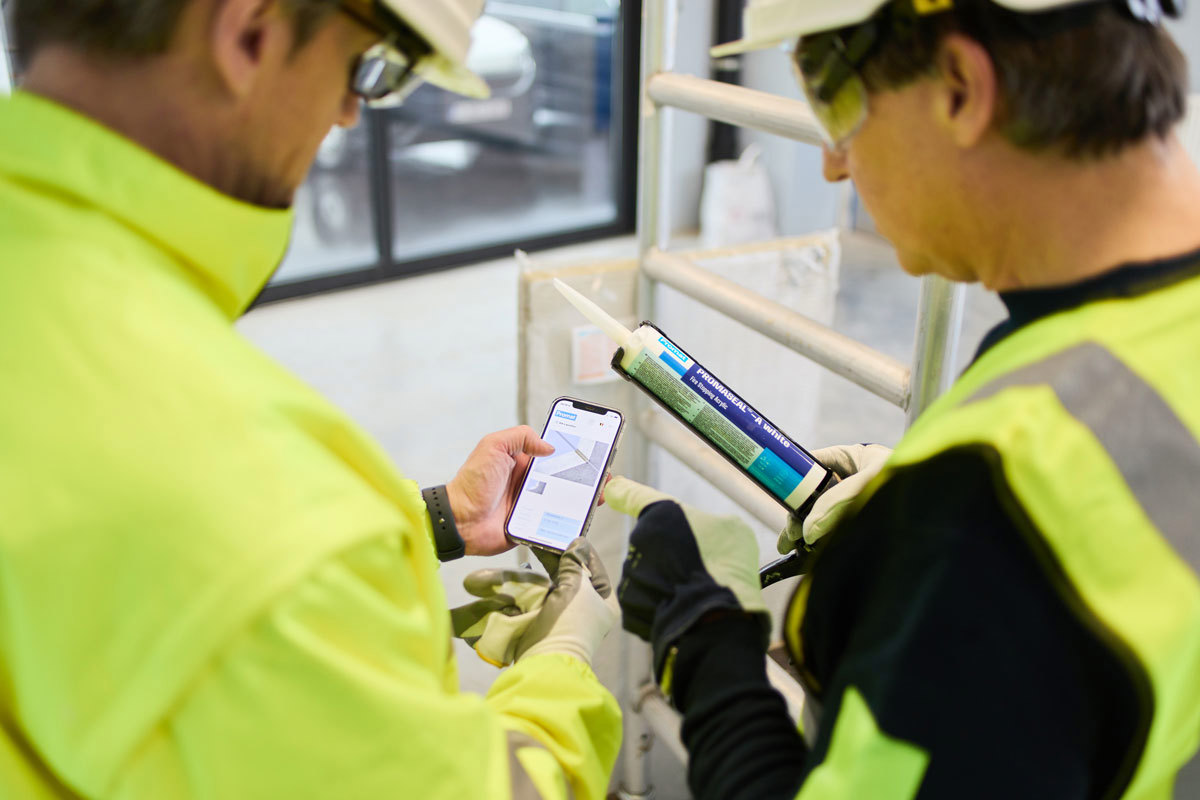 Man on the left is looking at Promat’s mobile Firestopping Selector® App. The other man is holding a pack of sealant.