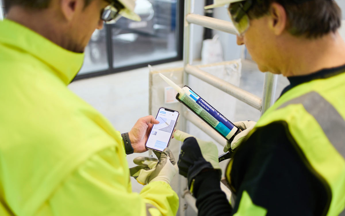 Man on the left is looking at Promat’s mobile Firestopping Selector® App. The other man is holding a pack of sealant.