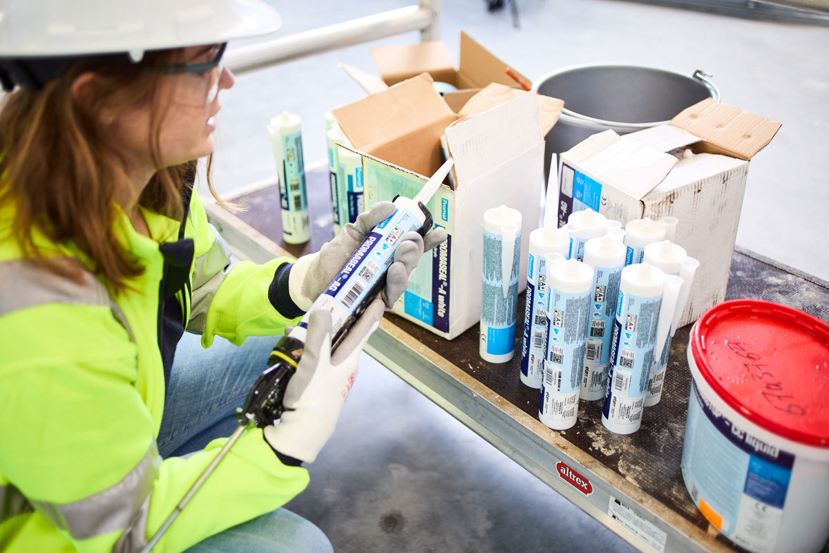 A woman installer reading the specifications on one of several sealant product and brand varieties before her.