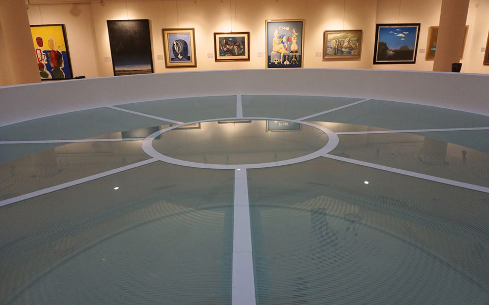 Záber zblízka na architektonický sklenený element v galérii Nedbalka, v pozadí vystavené obrazy