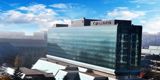 Mogočna steklena zunanjost hotela Crowne Plaza Beograd, v ozadju se vidi stavbe mesta in modro nebo. 