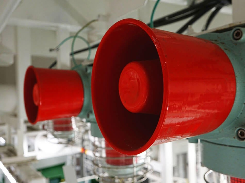 Zdjęcie przedstawiające dwa czerwone głośniki syren alarmowych. Pierwsza syrena jest po prawej stronie, dalej, bardziej w tle po lewej stronie znajduje się druga syrena.