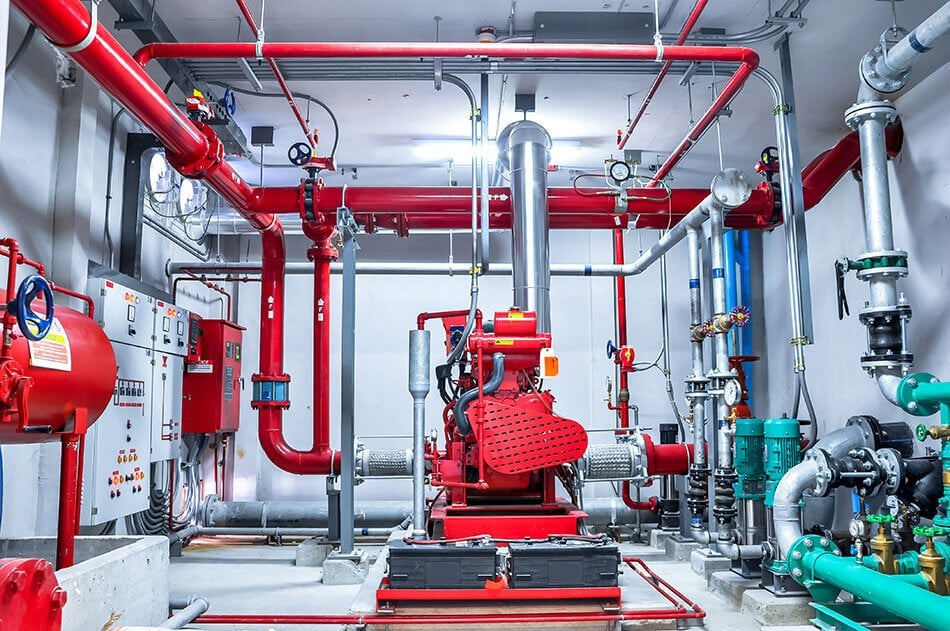 Zdjęcie przedstawiające skomplikowany system przeciwpożarowy. Na środku kadru jest czerwono maszyna od której wychodzą na wszystkie strony czerwone i srebrne rury różnej grubości.