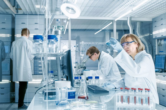 Na slici se vide naučnici kako rade u naučnoj laboratoriji koristeći epruvete, različita jedinjenja i specijalizovane uređaje
