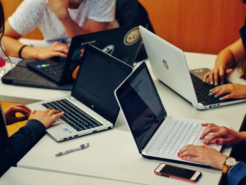 Imagine cu patru oameni stând la un birou, lucrând la laptopuri