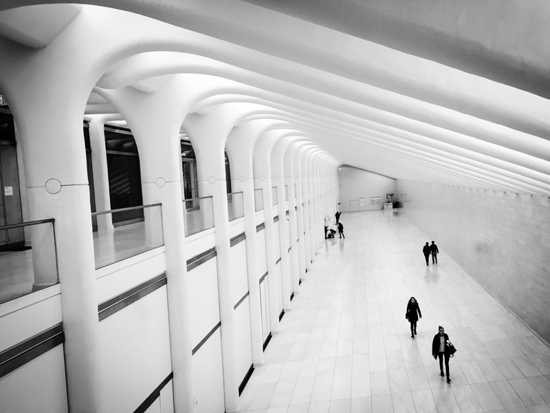 Bijela unutrašnjost One World Trade centra,. Desno je veliki hodnik u kojem hodaju ljudi, lijevo je hodnik na gornjem katu.