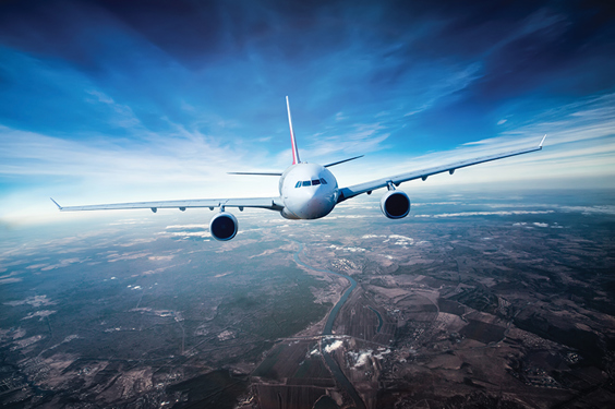 Čeoni pogled u avion u letu koji se nalazi iznad zelenih predela i brda, a iznad koga su plavo nebo i pojedini oblaci.