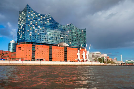 Slika prikazuje modernu arhitekturu objekta čiji je gornji deo zastakljen a krov talasast, a donji deo napravljen iz blokova.