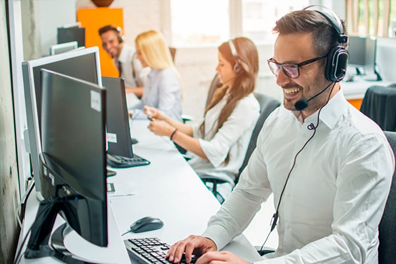 Muži a ženy sedia pri počítačoch v call centre so sluchátkami a mikrofónmi.
