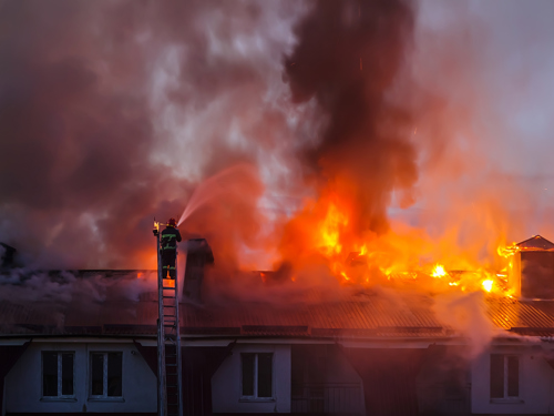 Vatrogasac gasi krov kuće iz kojeg izbija gusti crni dim i vatra.