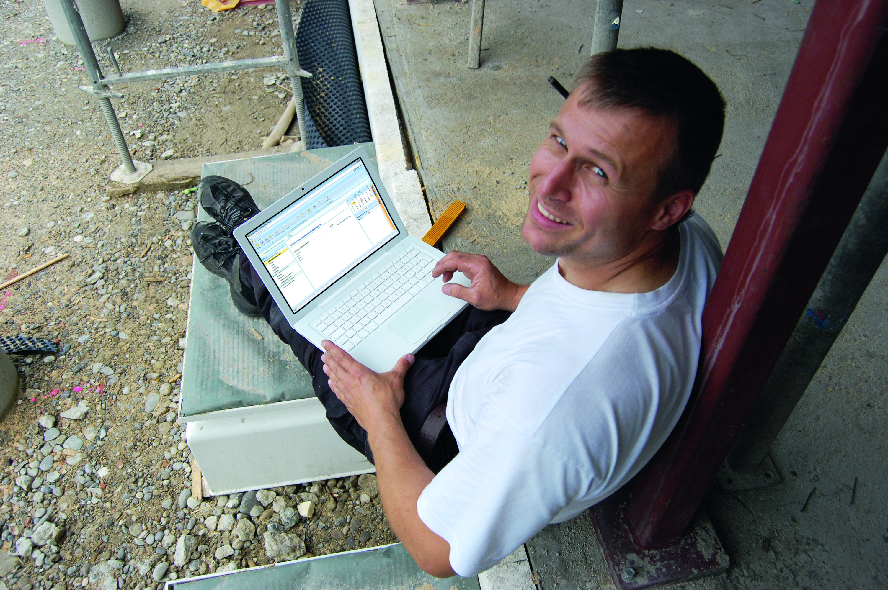 Radnik sjedi na gradilištu sa laptopom u krilu i otvorenom aplikacijom na zaslonu.
