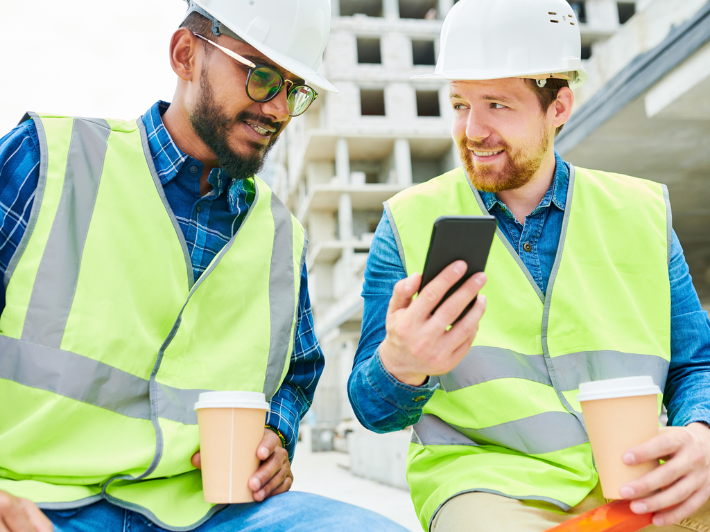 Fotografija dveh inženirjev na gradbišču, ki gledata v zaslon mobilnega telefona.