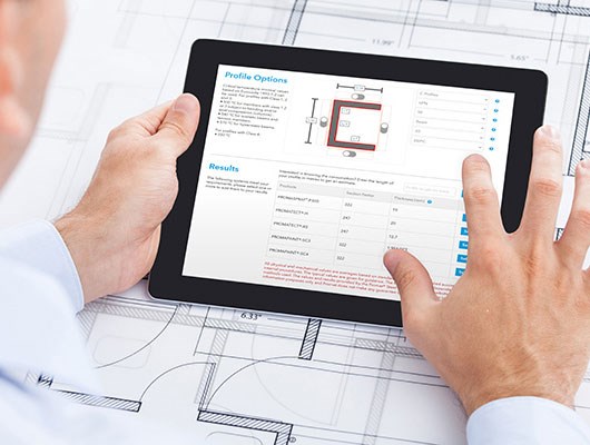 Jedan par ruku drži prijenosni tablet s web stranicom Promat i aplikacijom za planiranje gradnje. Ispod ploče je nacrt prostornog plana.