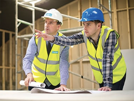 Promatovi eksperti u fluorescentnim prslucima i jednobojnim šlemovima nadgledaju radove u okviru građevinskog objekta.