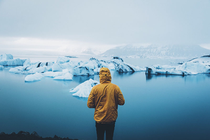 Persoană îmbrăcată în galben stând lângă apă într-un peisaj muntos cu gheță